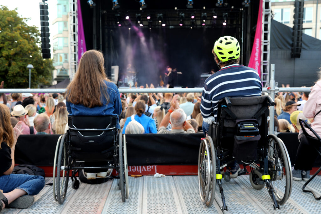 två personer i rullstol tittar på en konsert