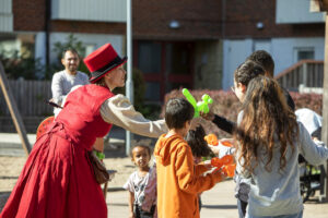 en person i röd klänning och röd höghatt delar ut ballongfigurer till barn