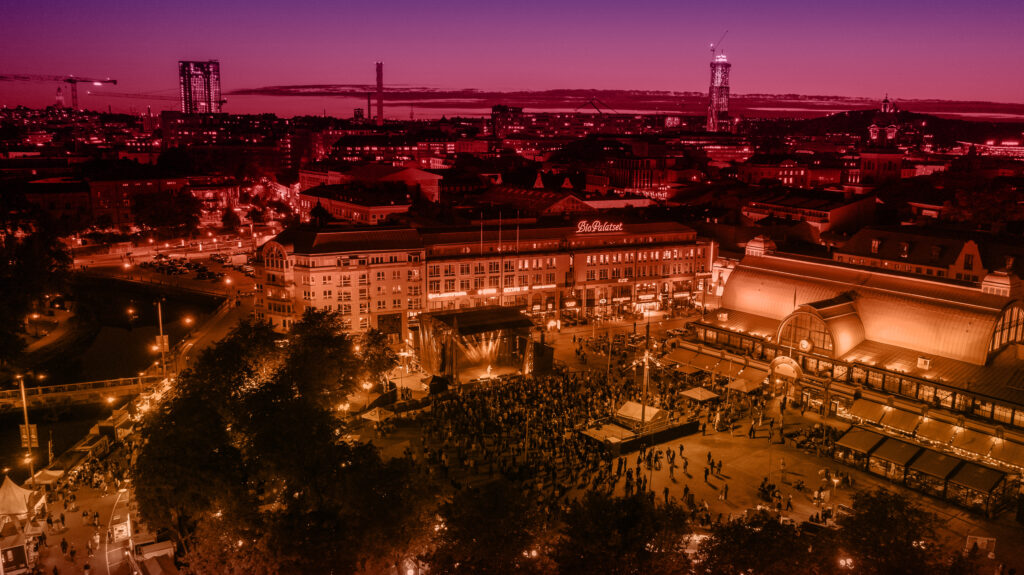 drönarfoto över kungstorget med Göteborgs stadssiluett i bakgrunden. bilden är redigerad med lila och orange färgfilter