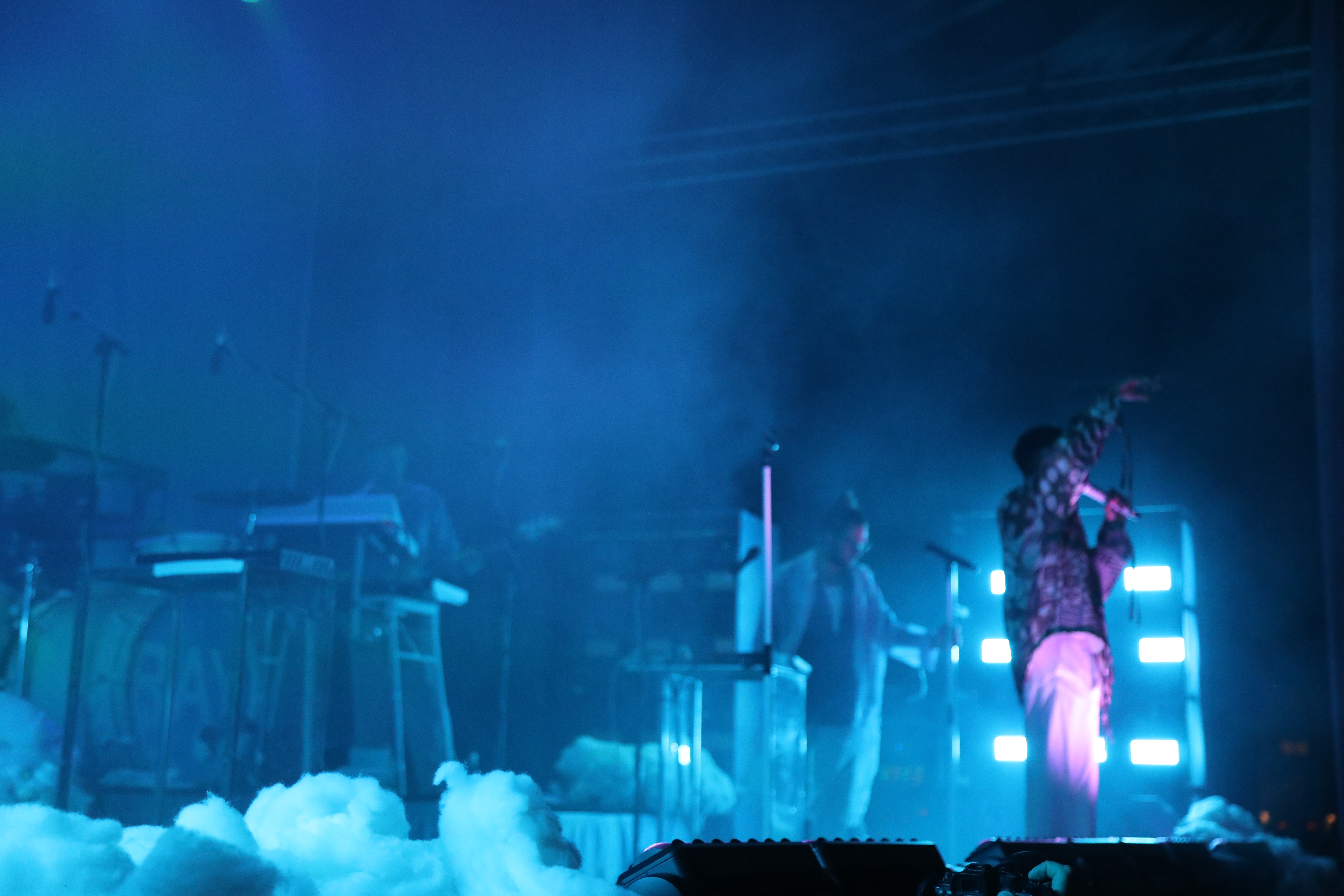 ett band spelar på en scen som är upplyst i blått ljus. bildens skärpa ligger på rök i förgrunden