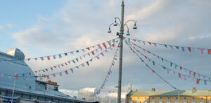 Färggrant flaggspel hänger åt flera håll från en lyktstolpe. Till vänster i bakgrunden anas Stora Saluhallens tak.